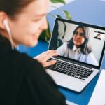 Woman having a video conference on a laptop, smiling and taking notes.